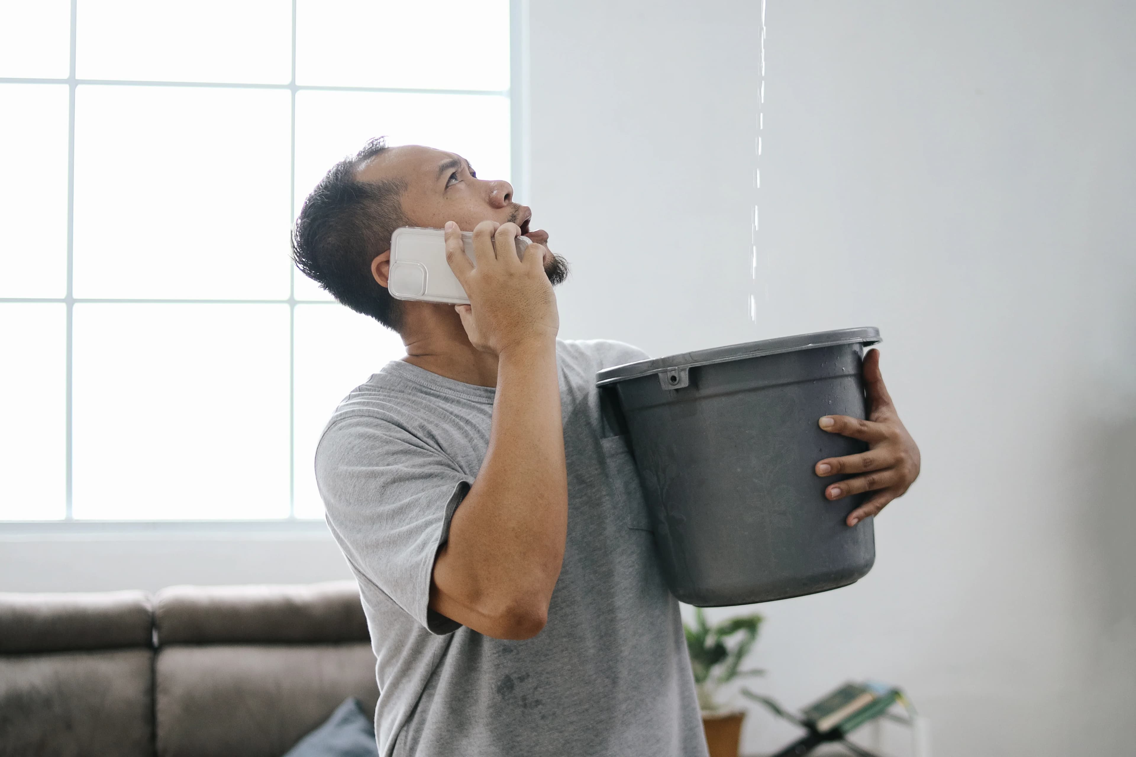 Man Catching Ceiling Leak In Bucket